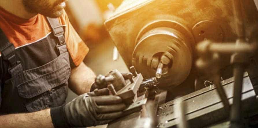 "Metal worker with work wear and gloves is turning metal on a lathe"