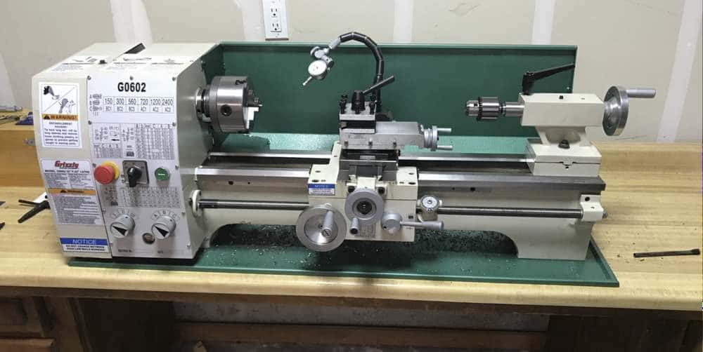 "a green colored grizzly G0602 metal lathe on a wooden benchtop"