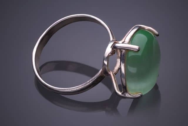 "a metal ring with a green stone lying in a glass floor "