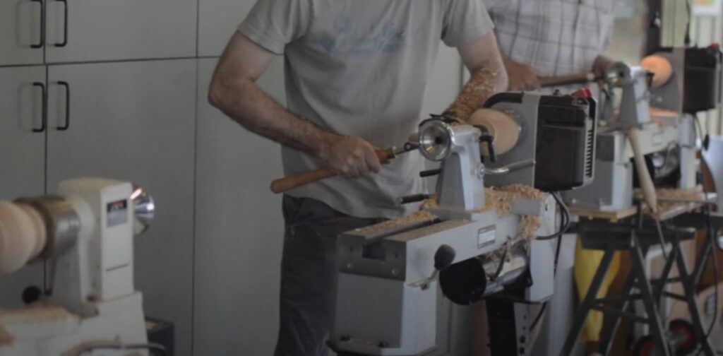 "two men practicing on white lathe machine with chisels in hand"
