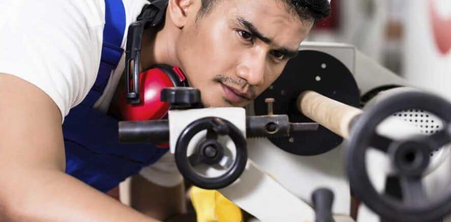 "Man wearing white and blue t-shirt is checking a white mini wood lathe during work"