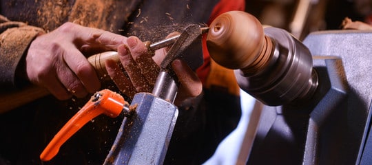 "Man's hand with a chisel turning small door knob on a wood lathe"