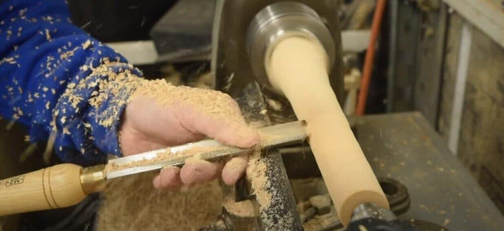 "man scraping woods with a chisel in hand after buying wood lathe" 