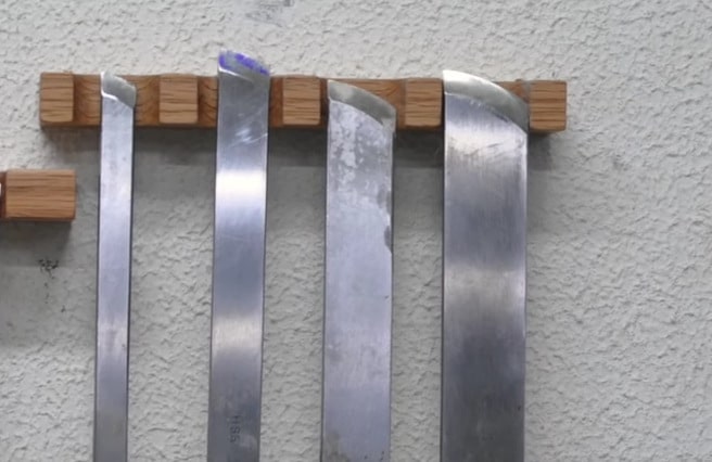 "Four skew chisels hanging on a wooden hanger into a white wall"