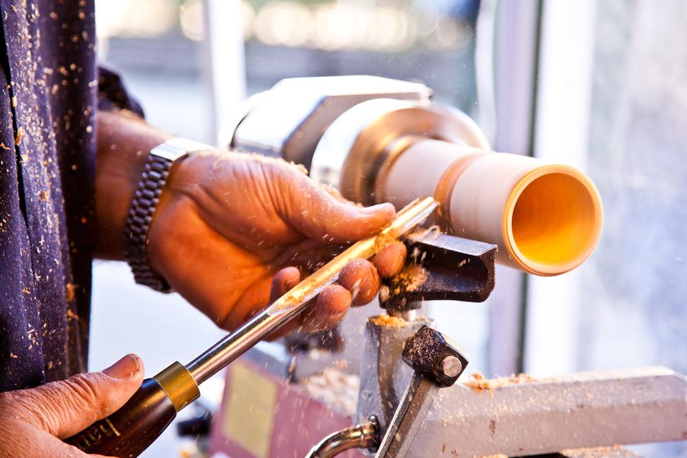 "Man with a chisel in hand turning spindle on a wood lathe"