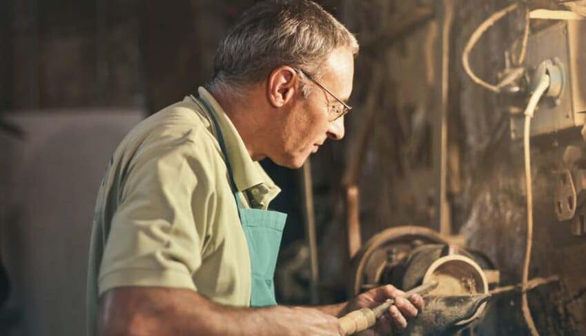 "Old male turner working on lathe machine in workshop"