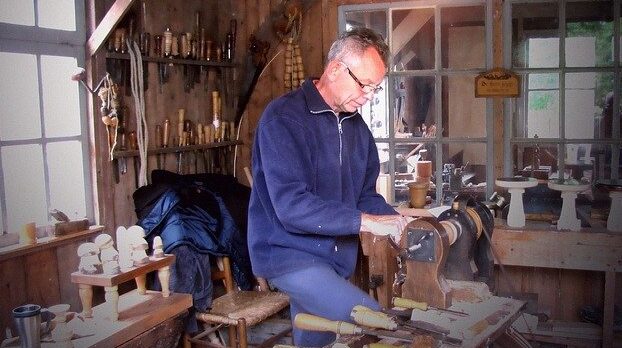 "old man in blue shirt in a woodworking garage and working with his lathe"