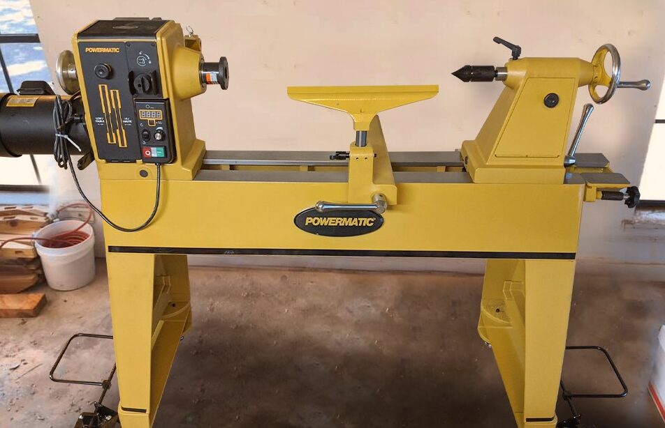 "Yellow colored powermatic wood lathe standing in front of a off white wall"