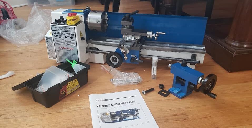"a blue color full set of mini metal lathe with parts and manual on a wooden benchtop"