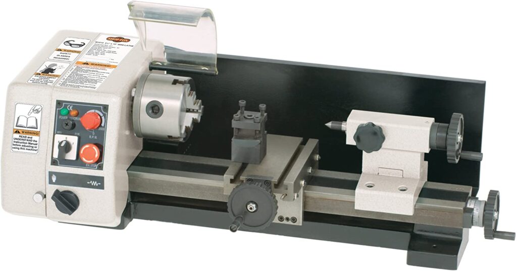 "A black and grey colored small metal turning lathe machine a white background"